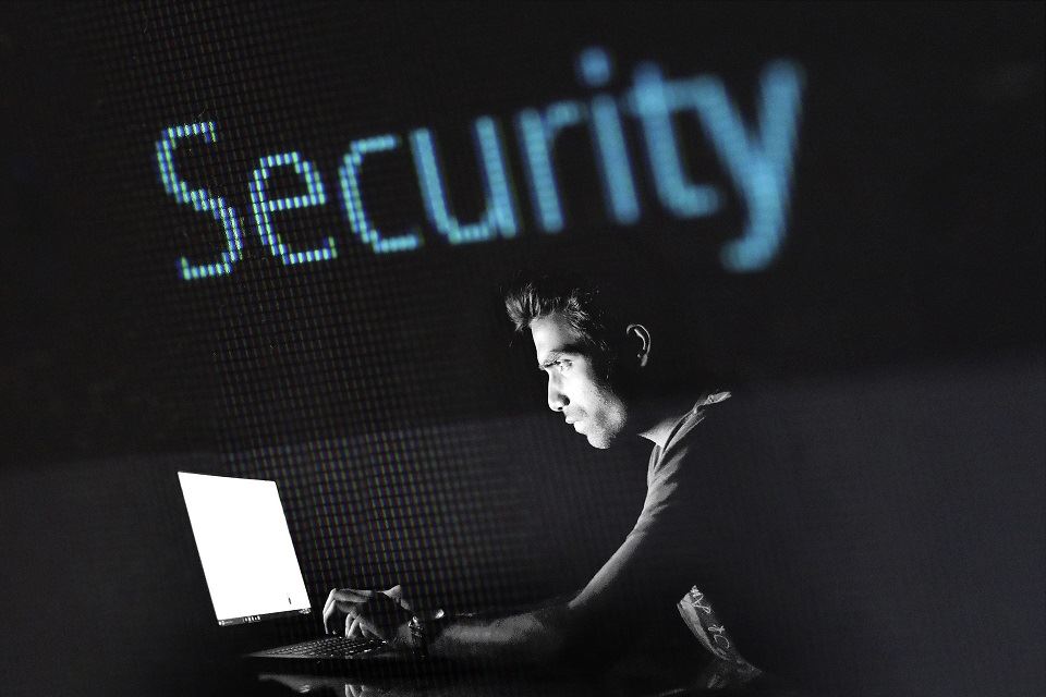 Man typing on a laptop in the dark. There is a blue animated font above his head spelling out Security