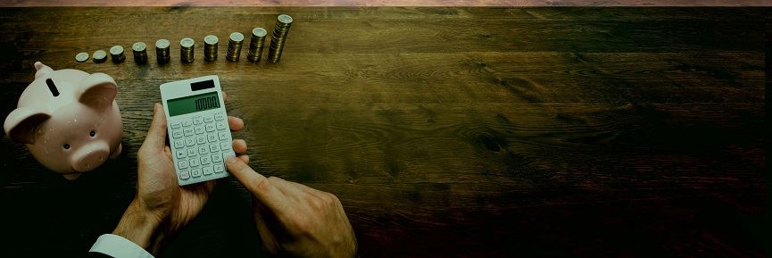 Piggy bank, coins stacked and a man typing on a calculator. The bank and coins are sitting on a table